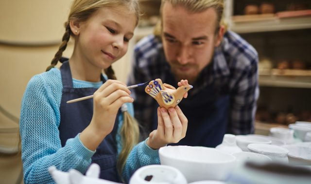 Cute girl painting clay toys and figures with her father near by
